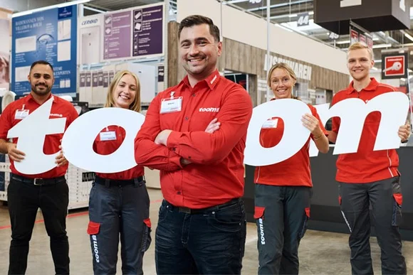 Fünf Toom Mitarbeiter in roter Arbeitskleidung halten die Buchstaben T O O M hoch